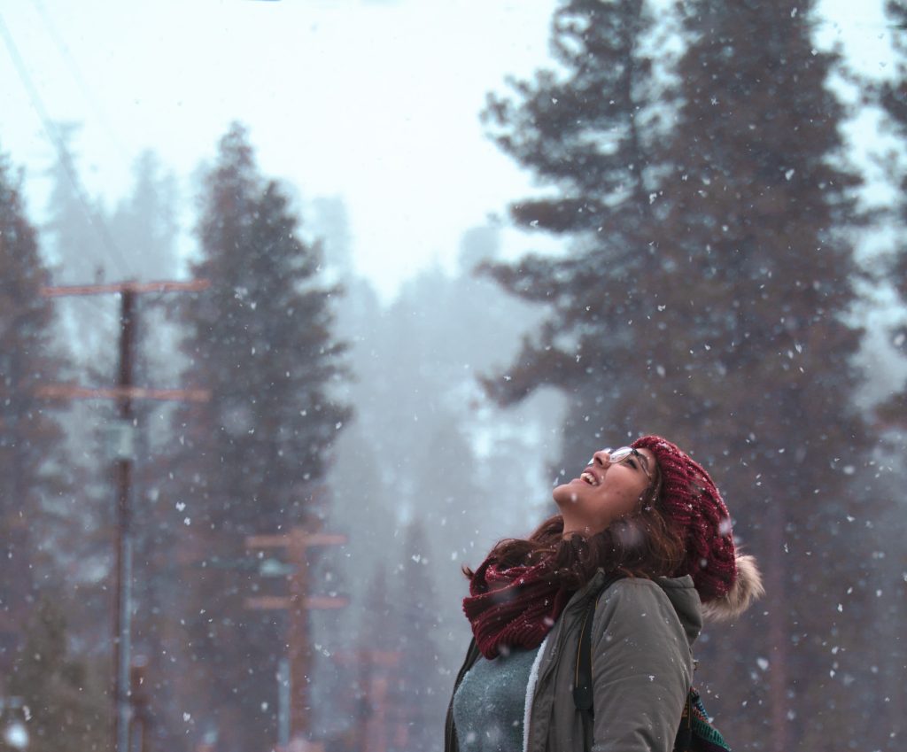 Close up of a women looking up to the sky smiling as snow falls down upon her.