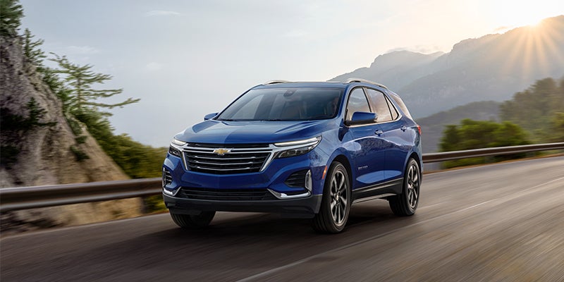 brand new blue 2023 Chevrolet Equinox driving down a mountainous highway.