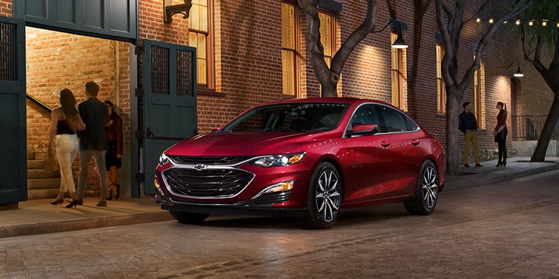 a brand new red 2023 Chevrolet Malibu Premiere parked downtown on a city cobbled street.